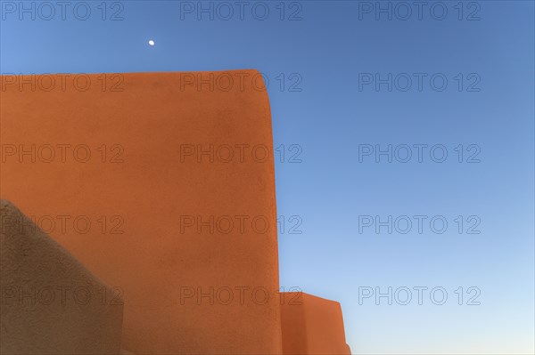 Moon in blue sky above adobe walls