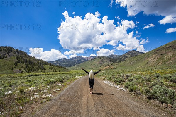 Rear view of senior woman standing with arms raised on road and looking at mountains