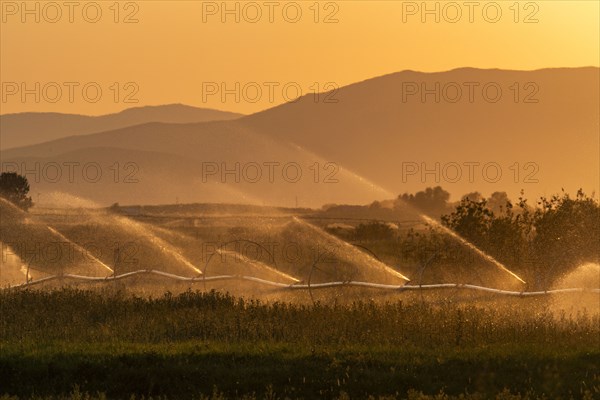 Farm irrigation system with mountain landscape in background at sunset