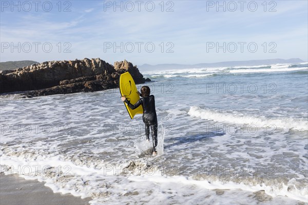 Boy entering Atlantic Ocean with body board in Kammabaai Beach