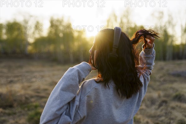 Rear view of woman listening to music in meadow at sunset