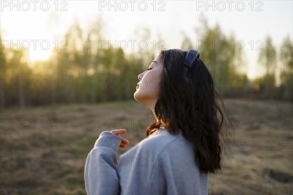 Side view of woman listening to music in meadow at sunset