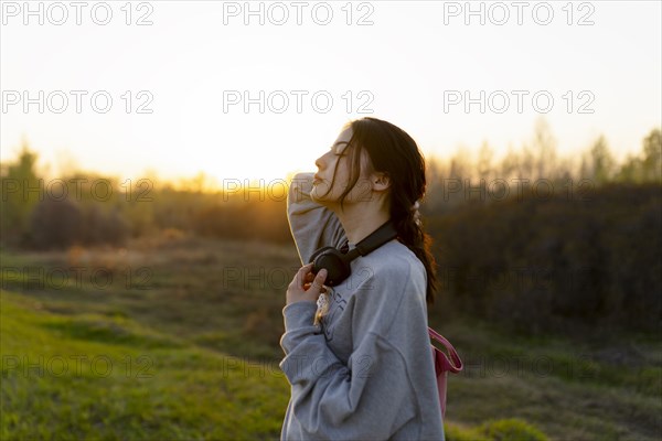 Portrait of young woman with headphones on meadow at sunset