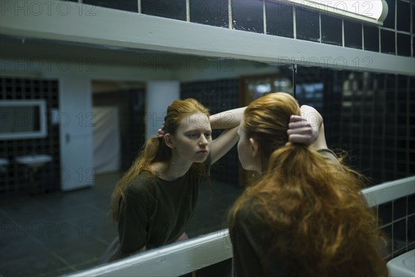 Young woman looking in mirror in public bathroom