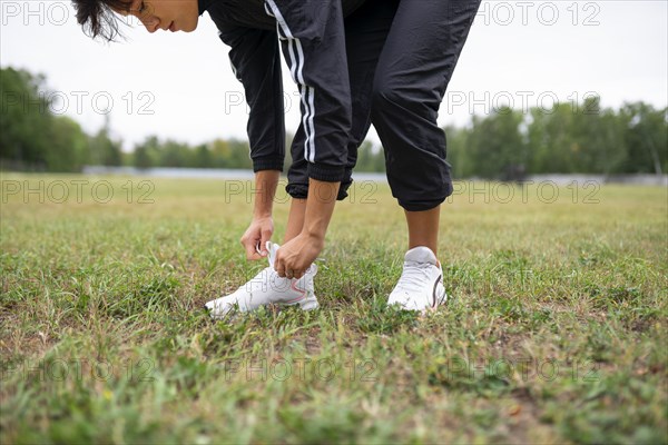 Young woman tying shoelaces while standing on grass
