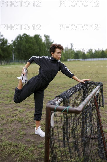 Young woman stretching legs while leaning on mini soccer goal