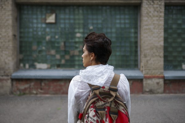 Rear view of young woman looking away while standing with backpack in city
