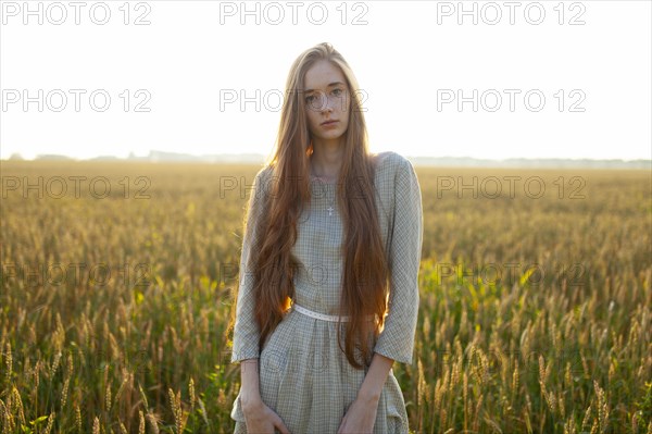 Portrait of young woman looking at camera while standing in field