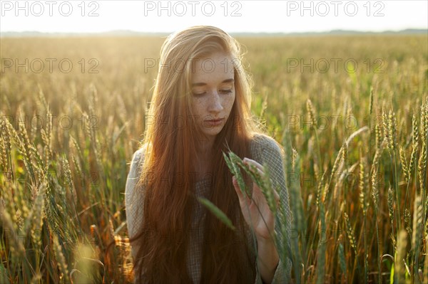 Portrait of young woman looking at cereal plants in field