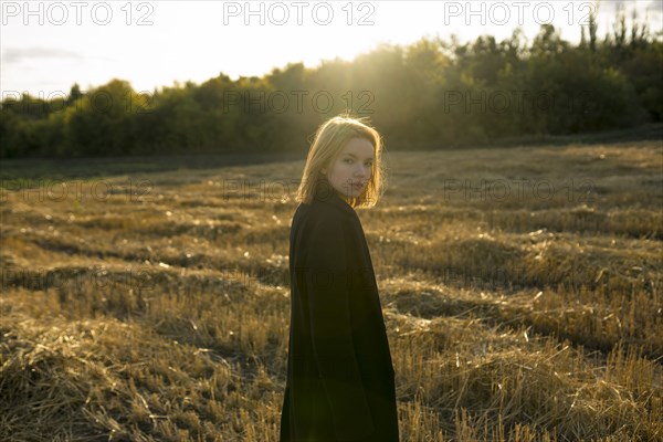 Portrait of young woman standing in field at sunset