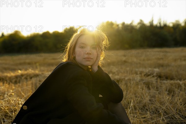 Portrait of young woman sitting in field at sunset