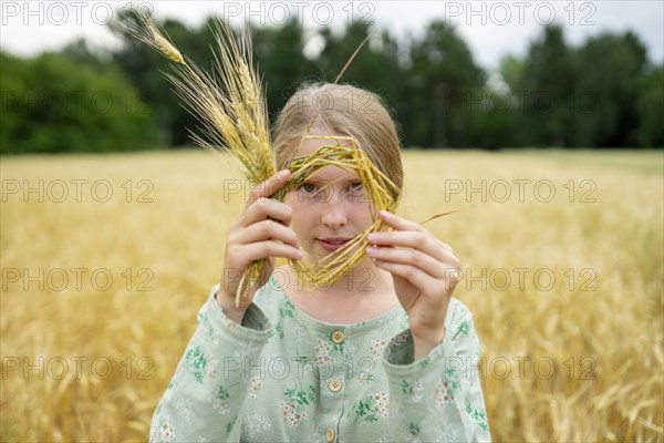Young woman holding small wreath of wheat in field