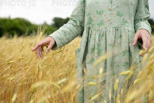 Young woman touching ears of wheat in field