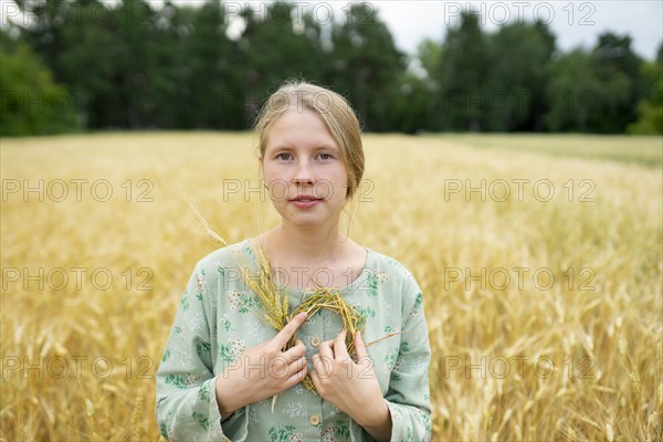 Portrait of young woman holding small wreath in wheat field