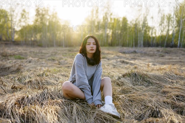 Brunette woman wearing grey sweatshirt sitting in meadow