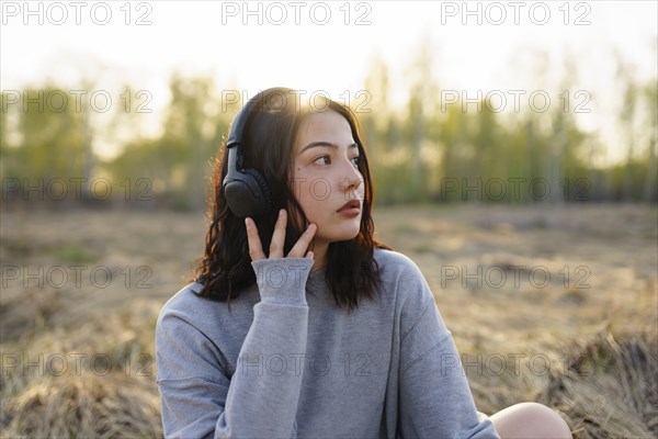 Young woman wearing headphones and sitting in meadow