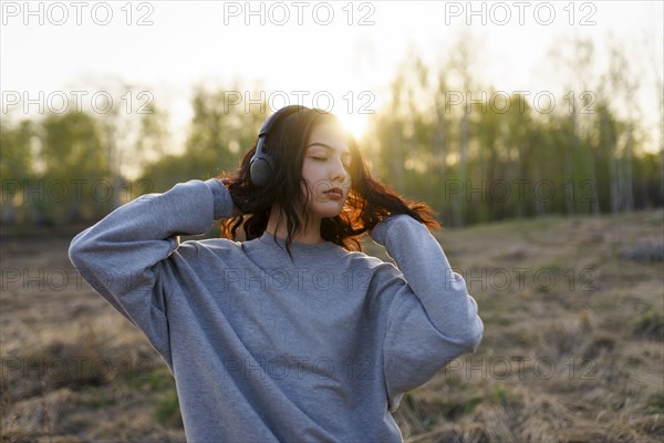 Portrait of woman listening to music with closed eyes in meadow at sunset
