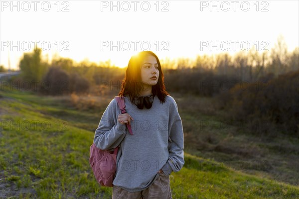 Woman wearing grey sweatshirt standing in meadow at sunset