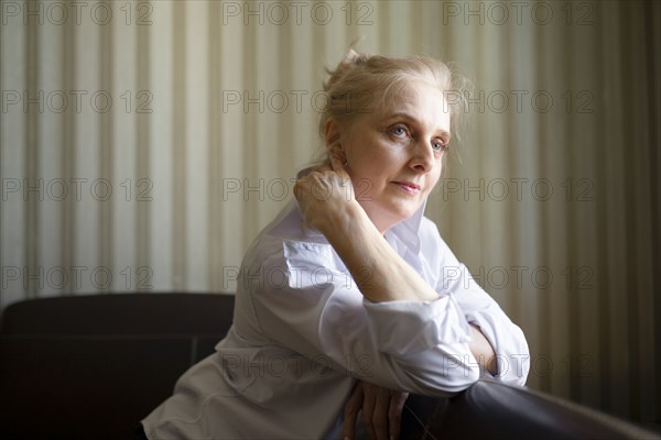 Woman leaning on sofa backrest and touching neck