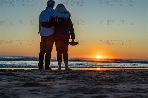 Rear view of couple standing at Cannon Beach at sunset