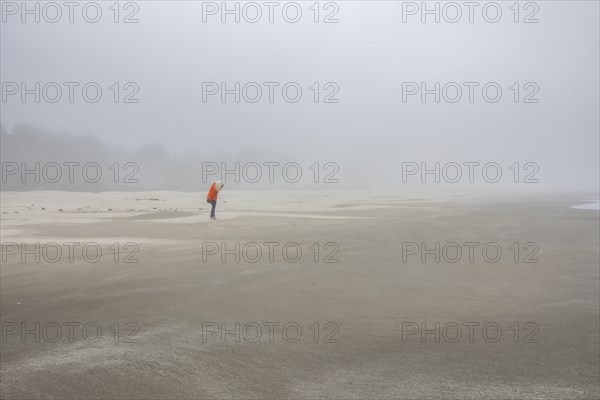 Woman in orange jacket standing on foggy beach