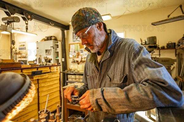 Senior artisan wood and metal craftsman works with tools in workshop