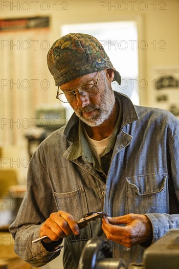 Senior artisan wood and metal craftsman works with tools in workshop