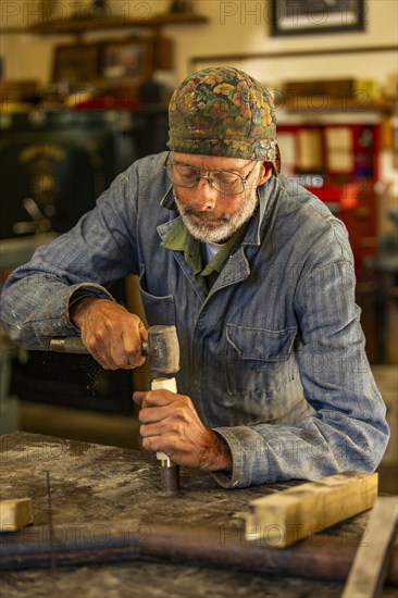 Senior artisan wood and metal craftsman works with tools in workshop