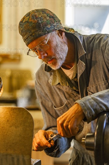 Senior artisan wood and metal craftsman works with tools in workshop