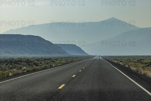 Empty highway leading through desert with mountains in background