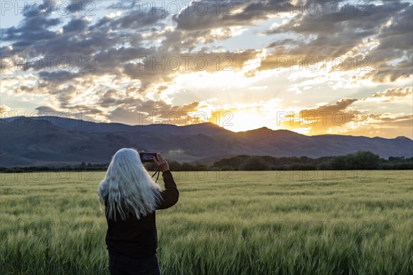 Senior woman photographing sunrise over mountains