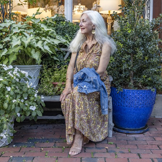 Senior blonde woman sitting on bench in shopping district