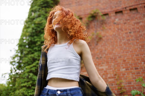 Redhaired woman posing next to old brick house