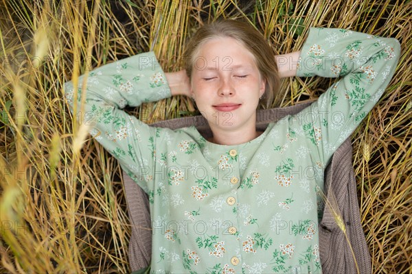 Young woman lying on crop with closed eyes in field