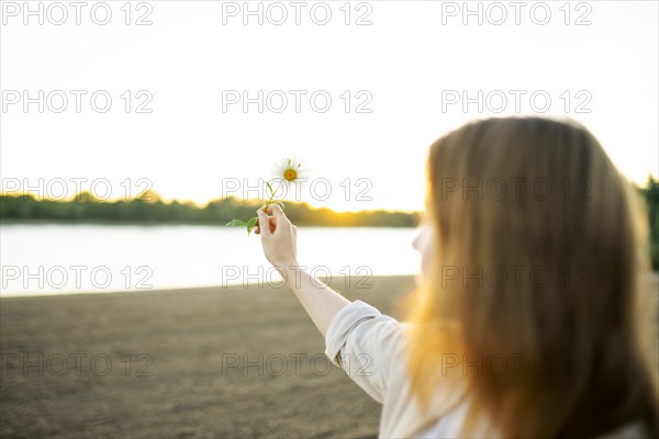 Woman holding chamomile flower on beach at sunset