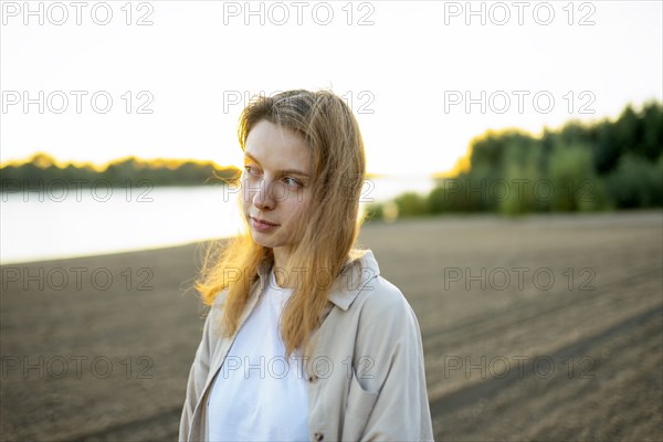 Portrait of thoughtful woman standing on beach at sunset