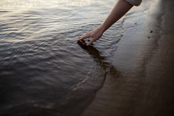 Close-up of woman touching water in river at sunset