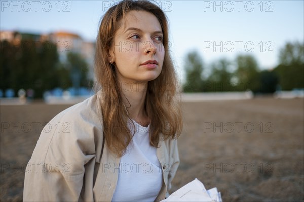 Portrait of thoughtful woman with book on beach