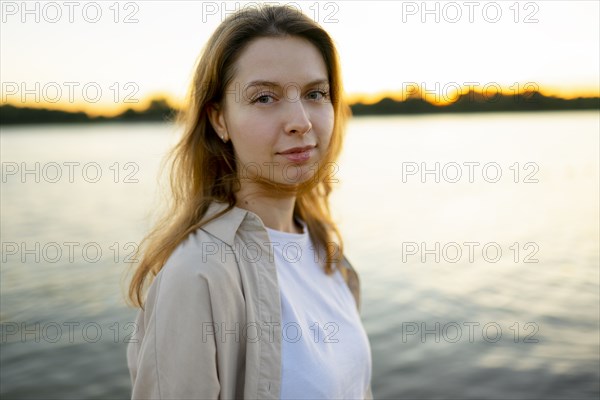 Portrait of thoughtful woman by river at sunset