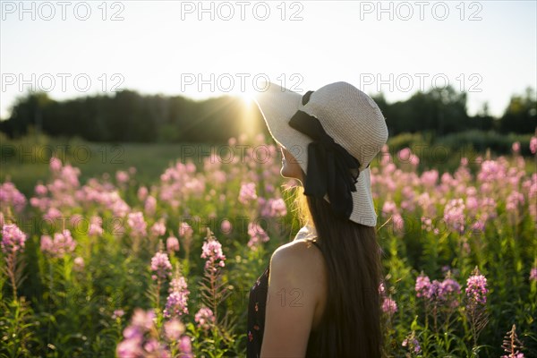 Young woman in straw hat standing in meadow on sunny day