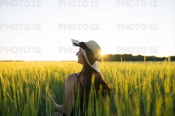 Rear view of woman in straw hat standing in field at sunset