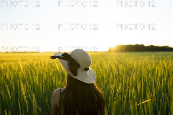 Rear view of woman in straw hat standing in field at sunset