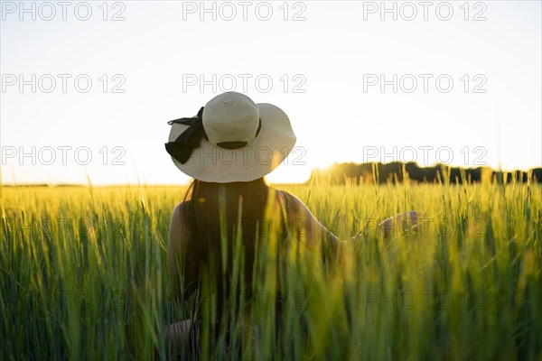 Rear view of woman in straw hat standing in field at sunset