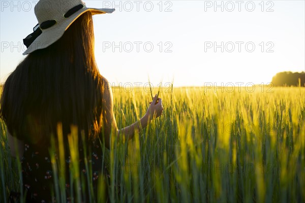 Rear view of woman in straw hat standing in field at sunset