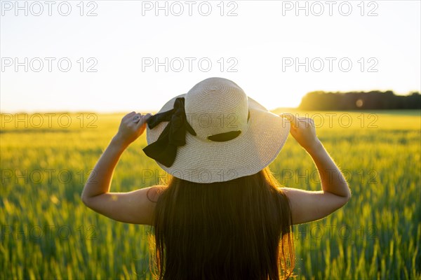 Rear view of woman in straw hat standing in field at sunset