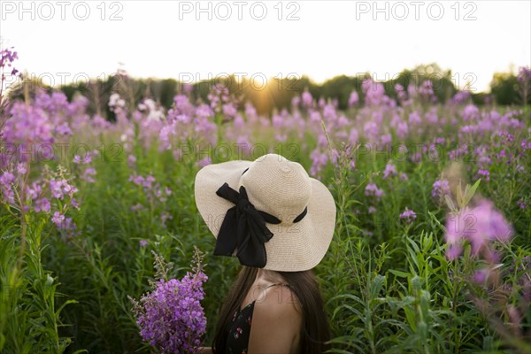 Side view of young woman looking at flowers on meadow