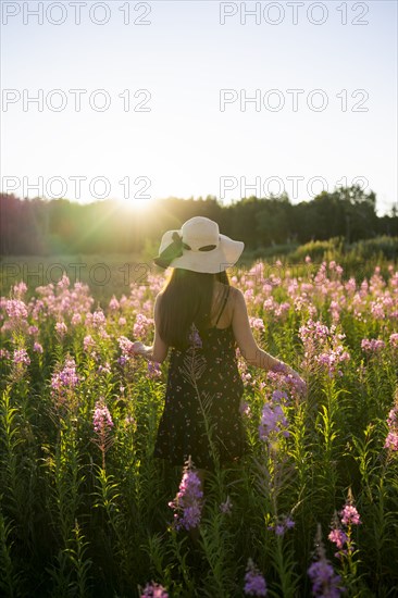 Rear view of woman in straw hat standing in meadow at sunset