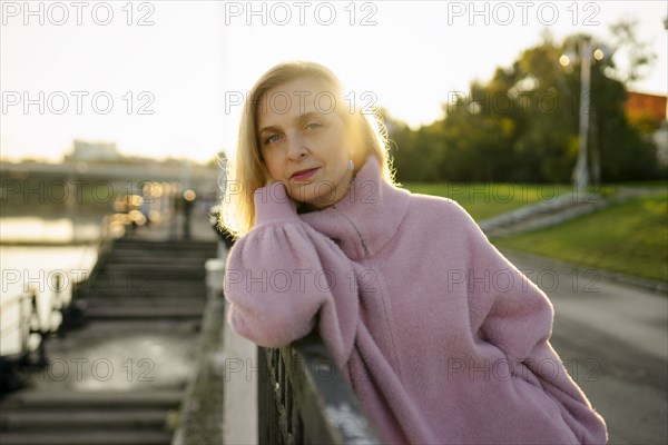 Portrait of serious woman leaning on railing at sunrise