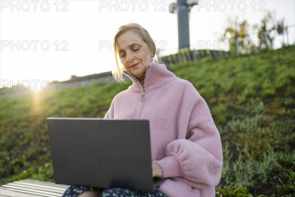 Woman working on laptop while sitting on bench at sunrise