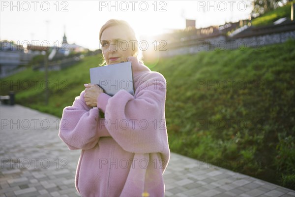 Woman embracing laptop while standing outdoors at sunrise